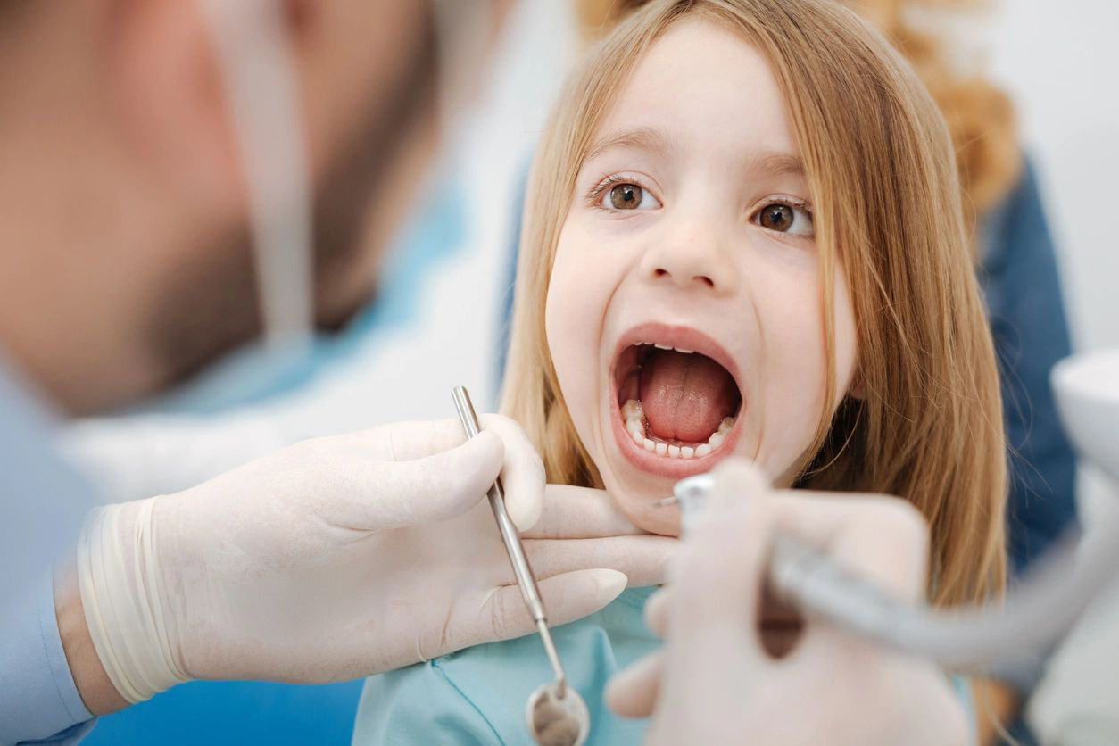 A little girl getting her teeth checked by an dentist.